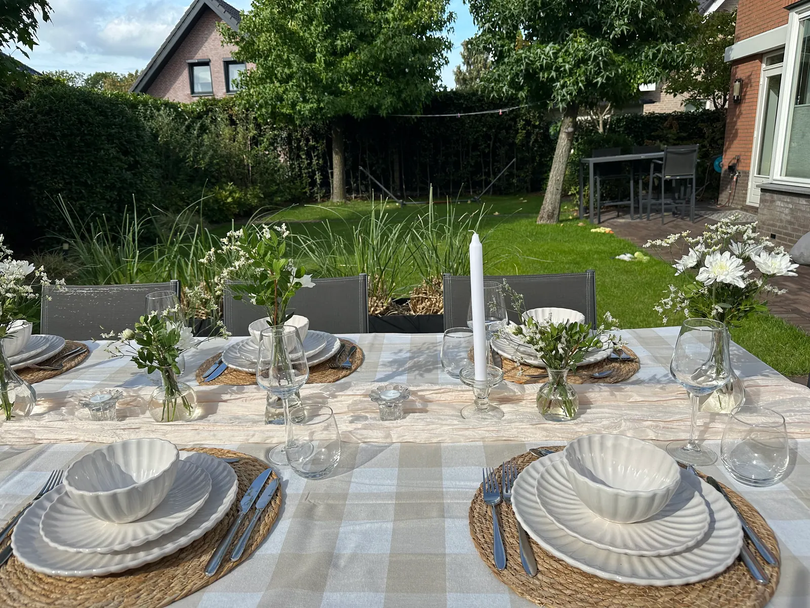 Gedekte tafel in de tuin met een beige geblokt tafelkleed en witte schalen
