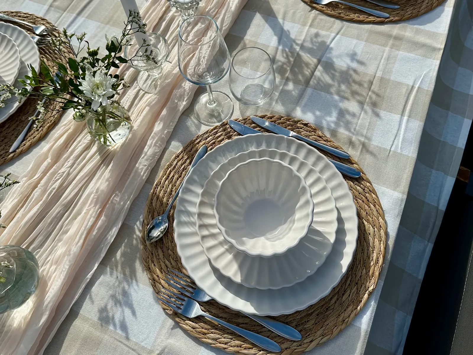 Witte geschulpte borden op rieten placemats met een lichte geblokte loper