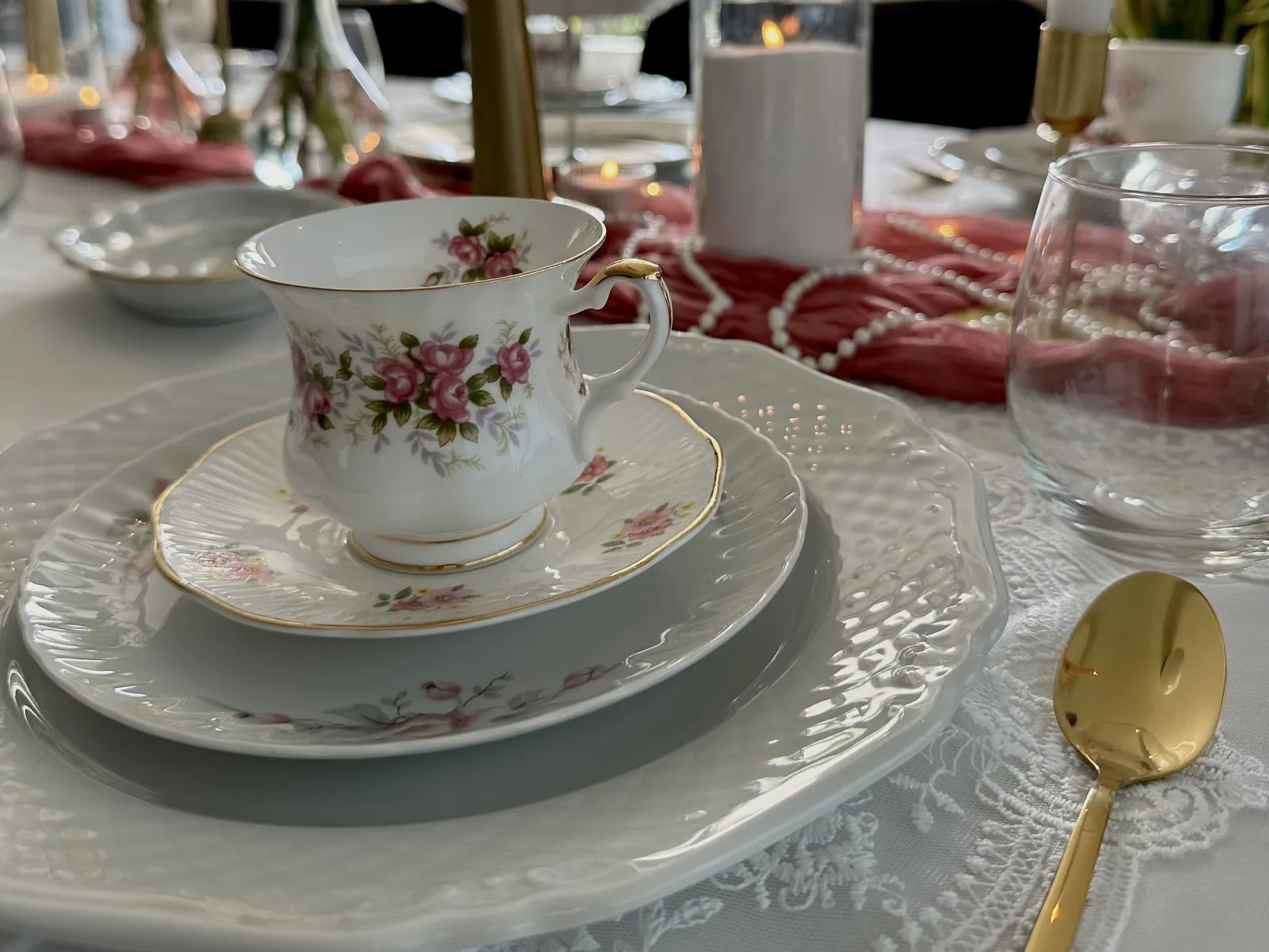 Theekopje met rozenprint op een schotel bij een afternoon tea met kanten tafelloper