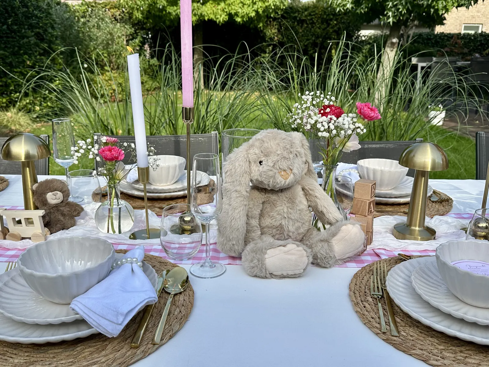 Roze babyshowertafel met een knuffelkonijn, gouden tafellampjes en roze bloemen