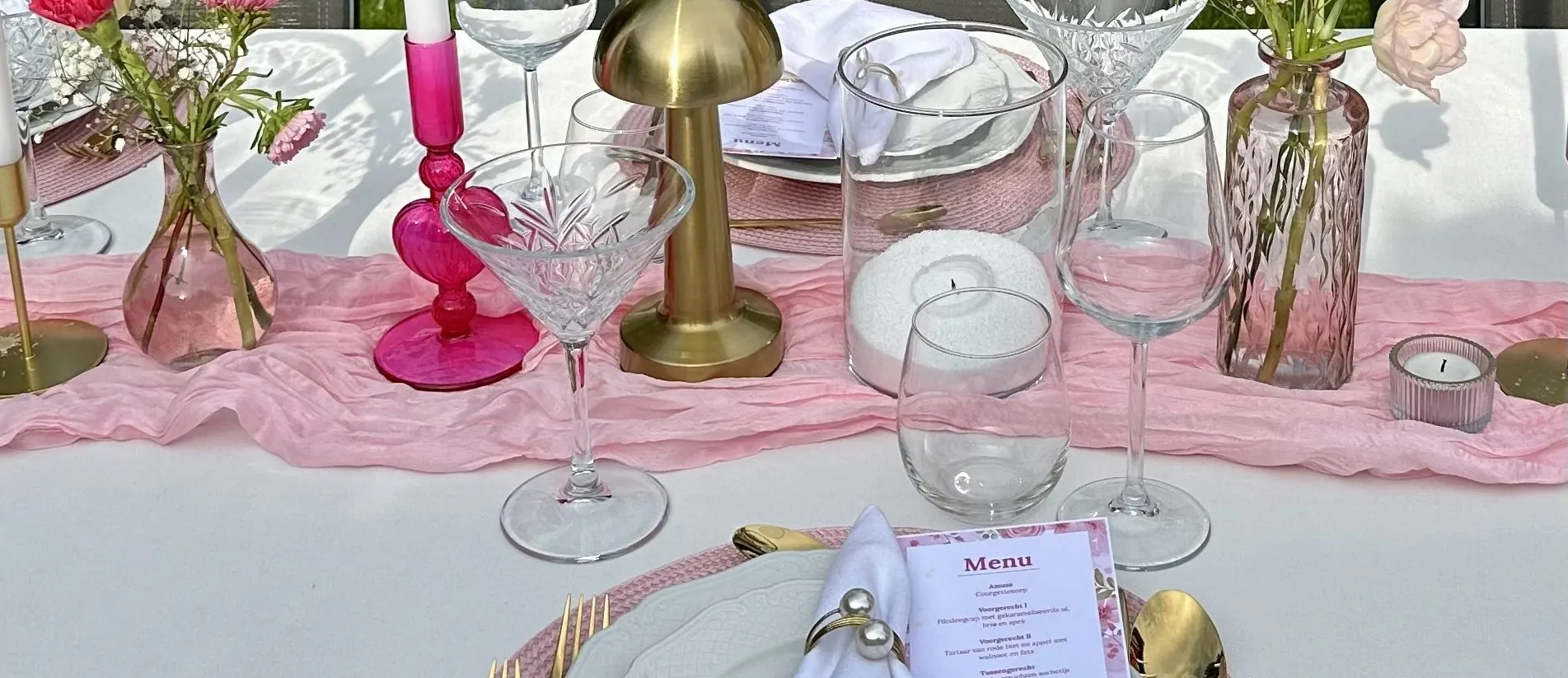 Roze tafel met roze kandelaars, een gouden tafellampje en een menukaart op het bord