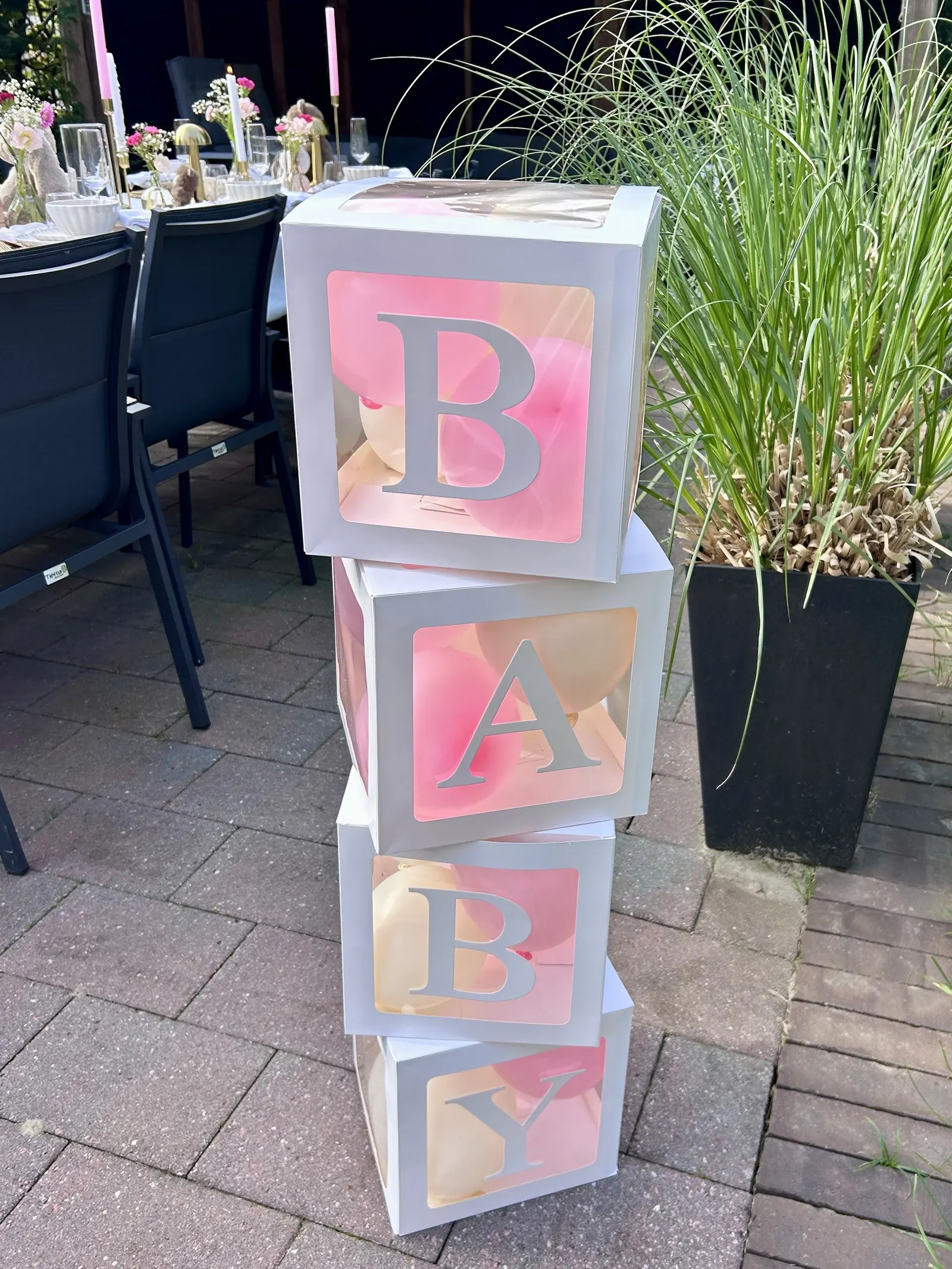 Gestapelde witte dozen met roze letters die samen BABY vormen, op een terras