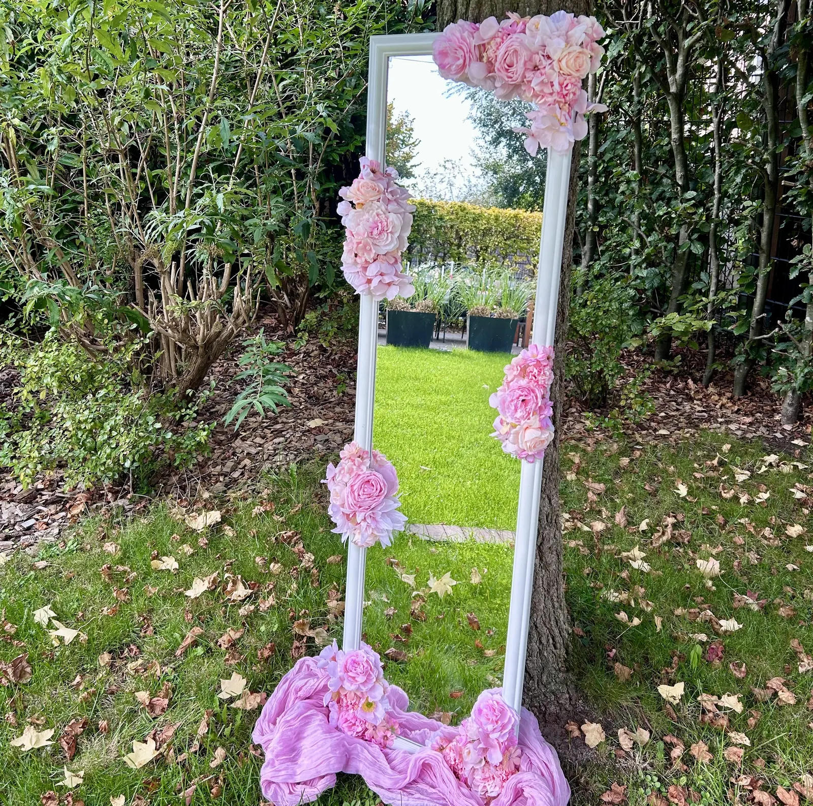 Staande witte spiegel versierd met roze bloemen, in de tuin