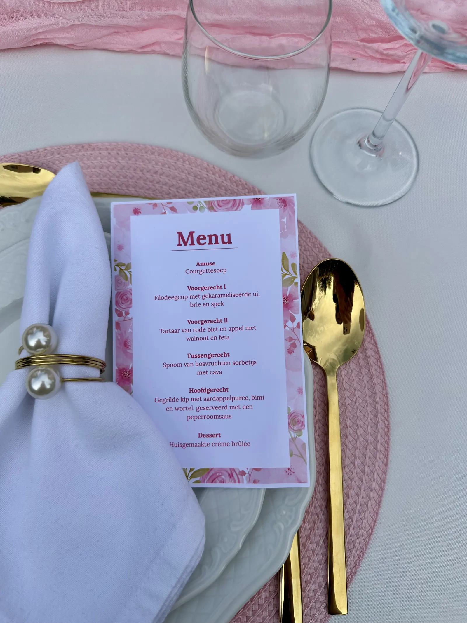 Menukaart met roze bloemen op een bord, naast een servet met parelservetring