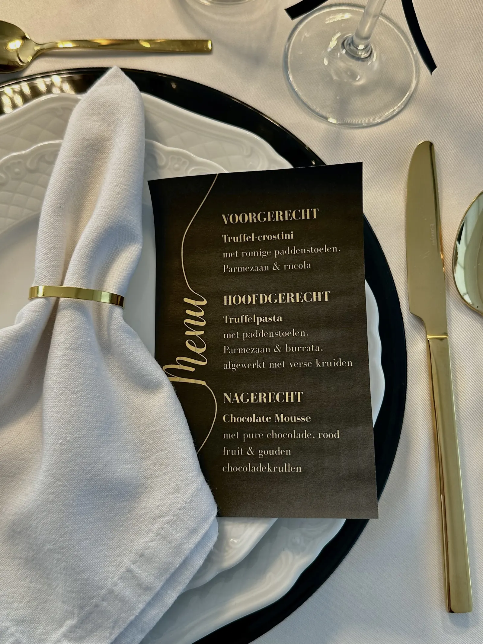 Zwarte menukaart met gouden letters naast een servet met gouden servetring
