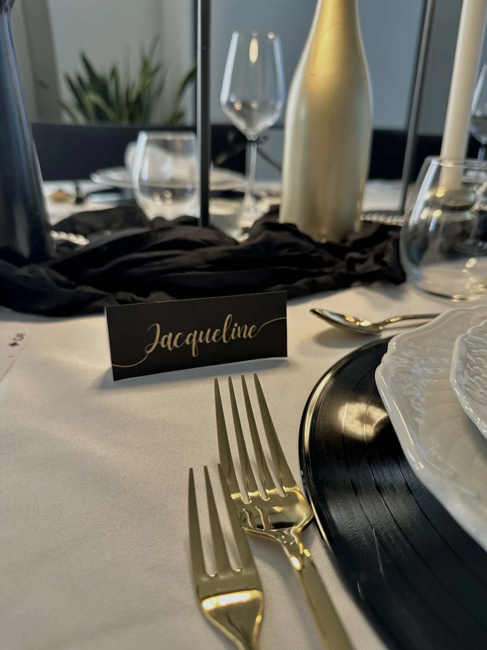 Zwart naamkaartje met de naam Jacqueline in gouden letters bij een bord op een vinylplaat