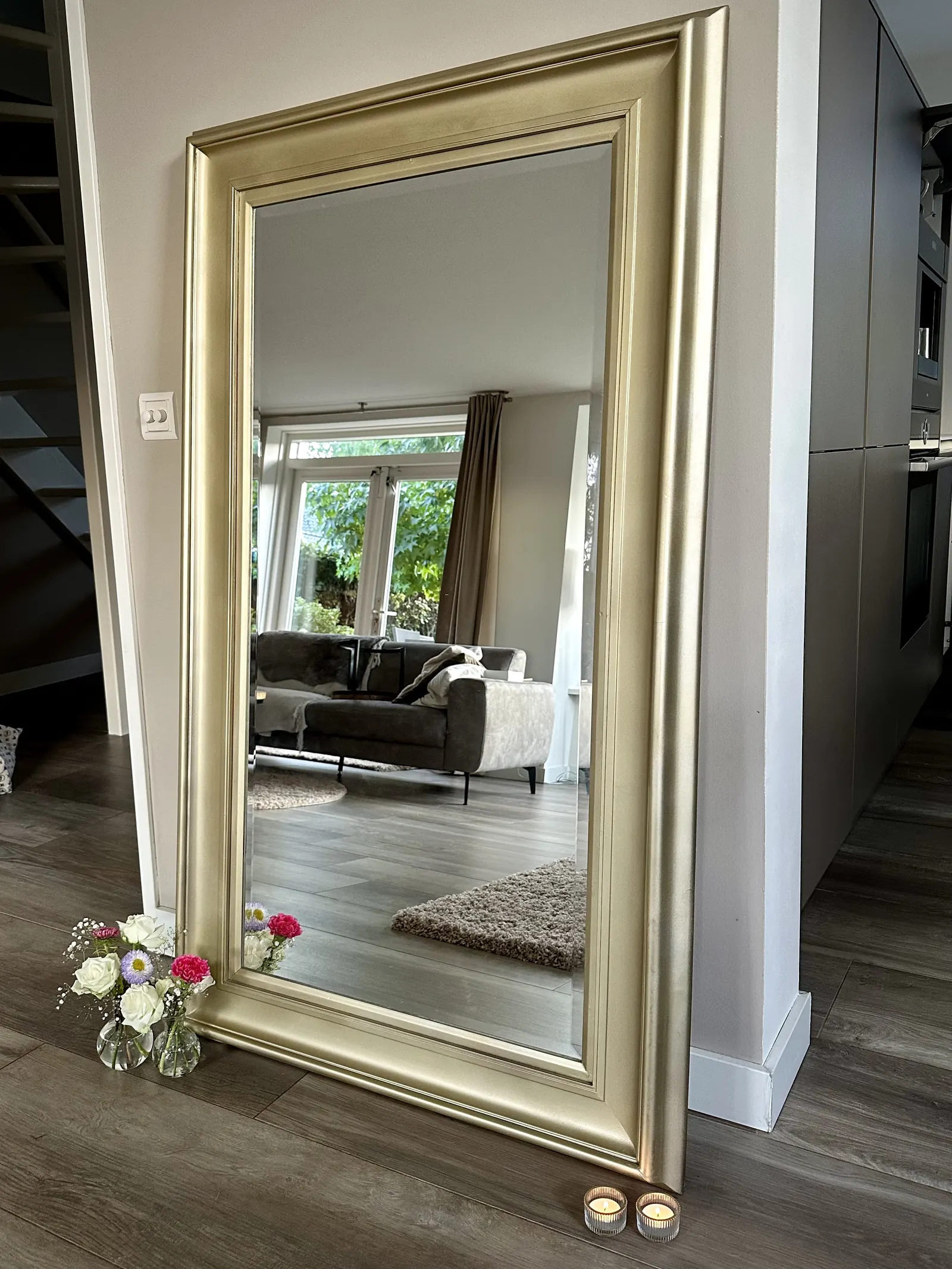 Grote spiegel met een gouden lijst in een woonkamer, met kleine vaasjes bloemen ervoor