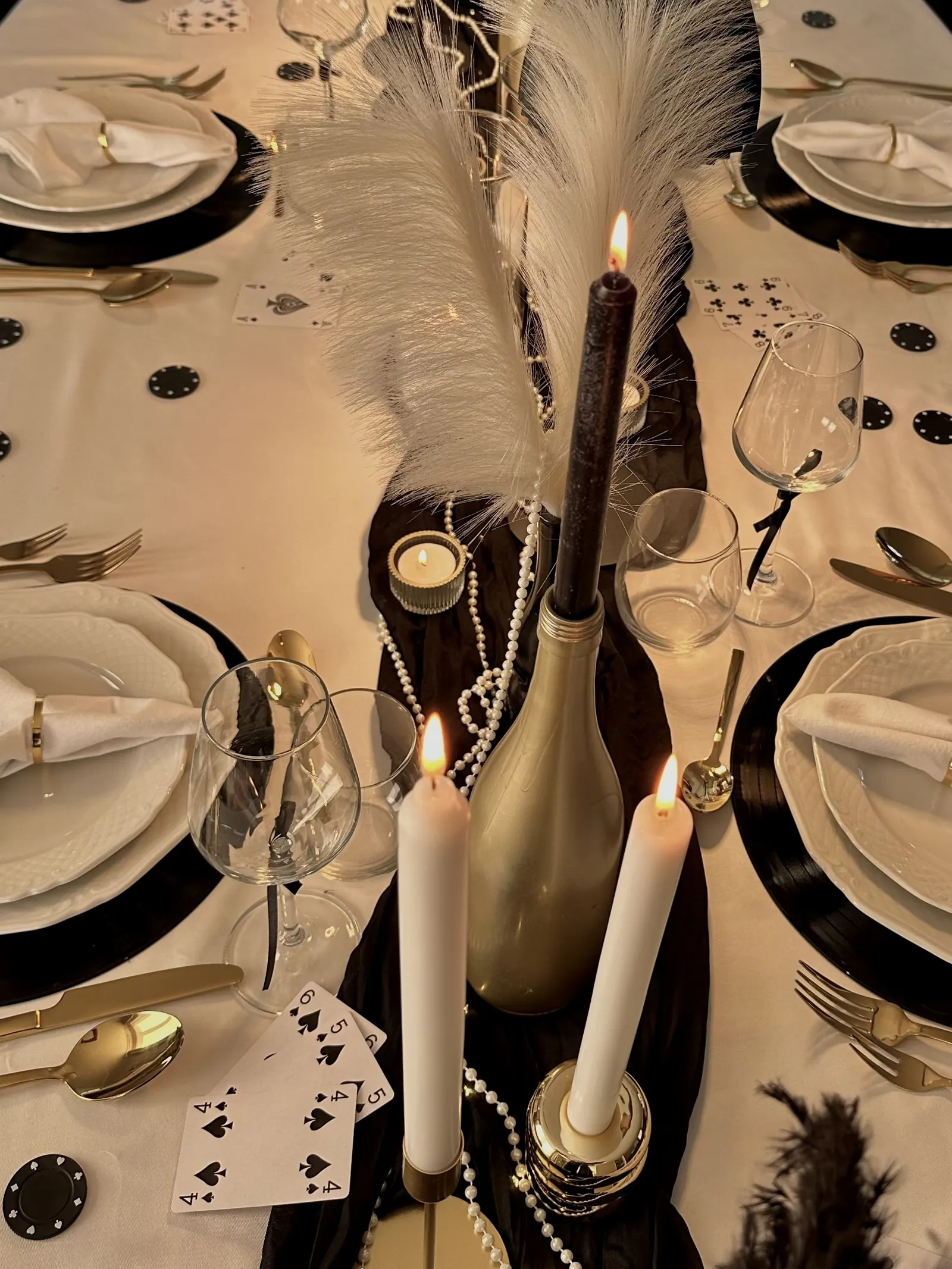 Gouden fles, witte kaarsen en een witte veer tussen de borden op de zwart met gouden tafel