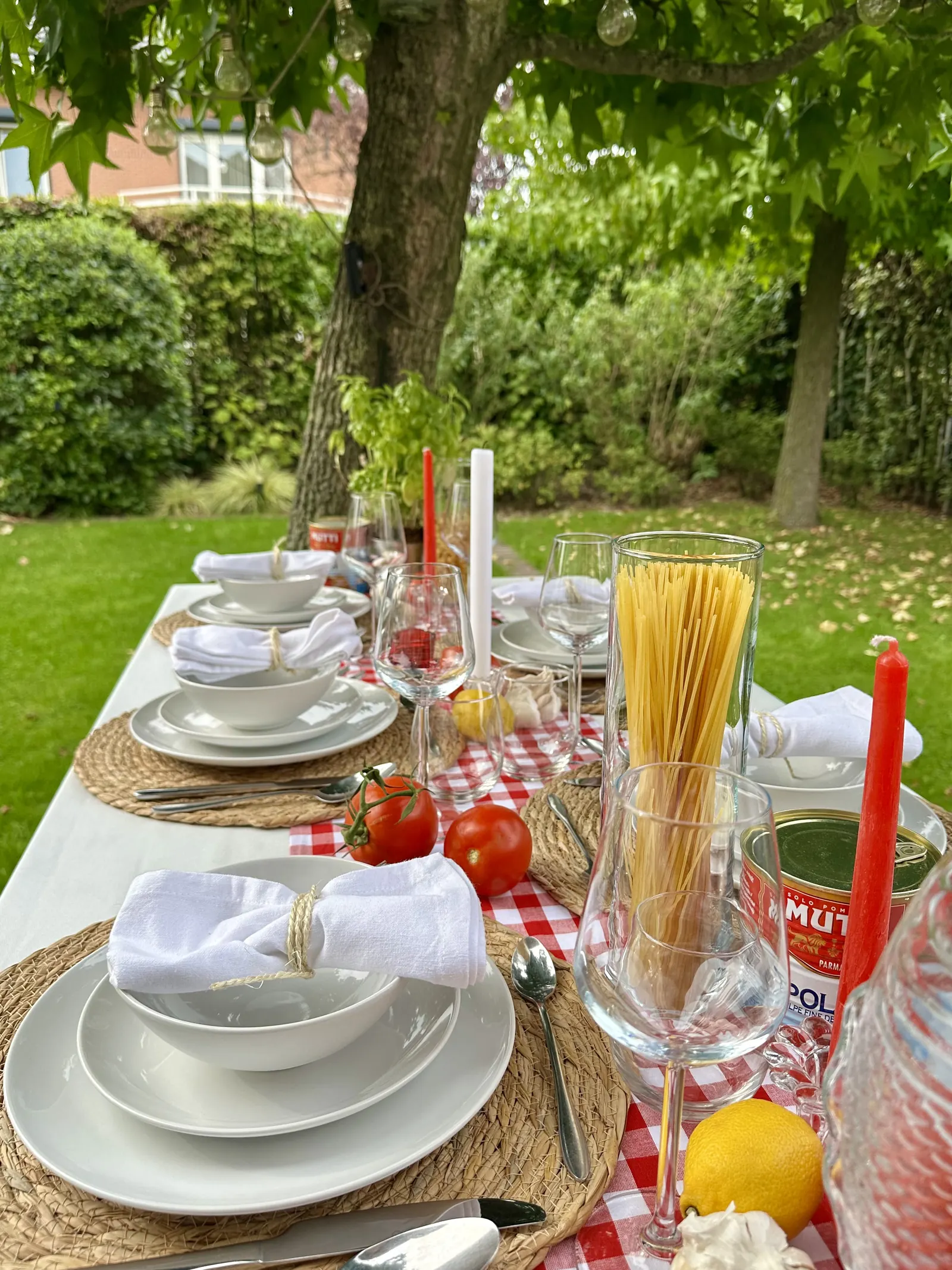 Italiaanse tafel in de tuin met spaghetti, tomaten, een citroen en rode kaarsen