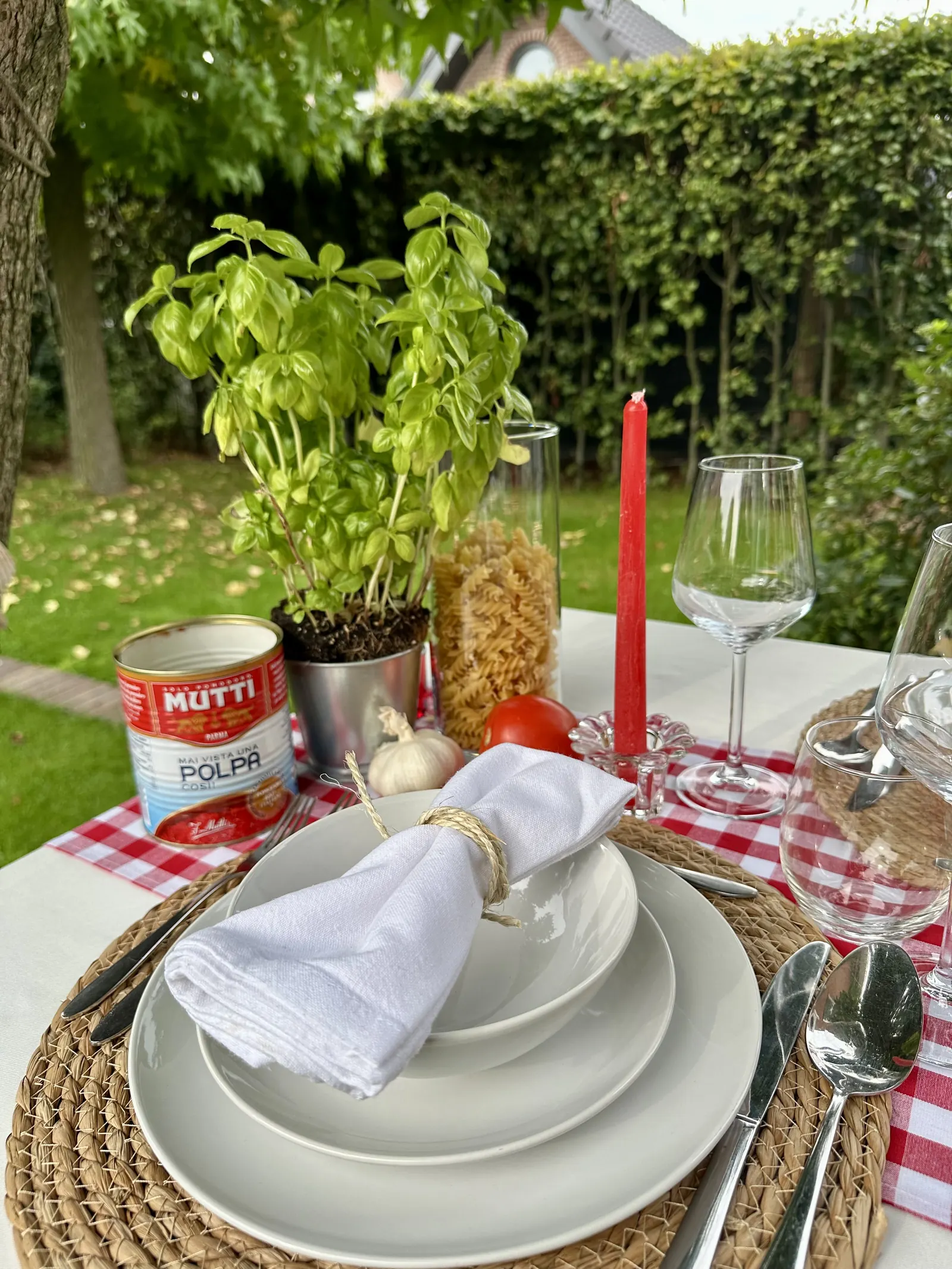 Basilicumplantje, een blik tomaten en pasta in een pot naast een gedekt bord