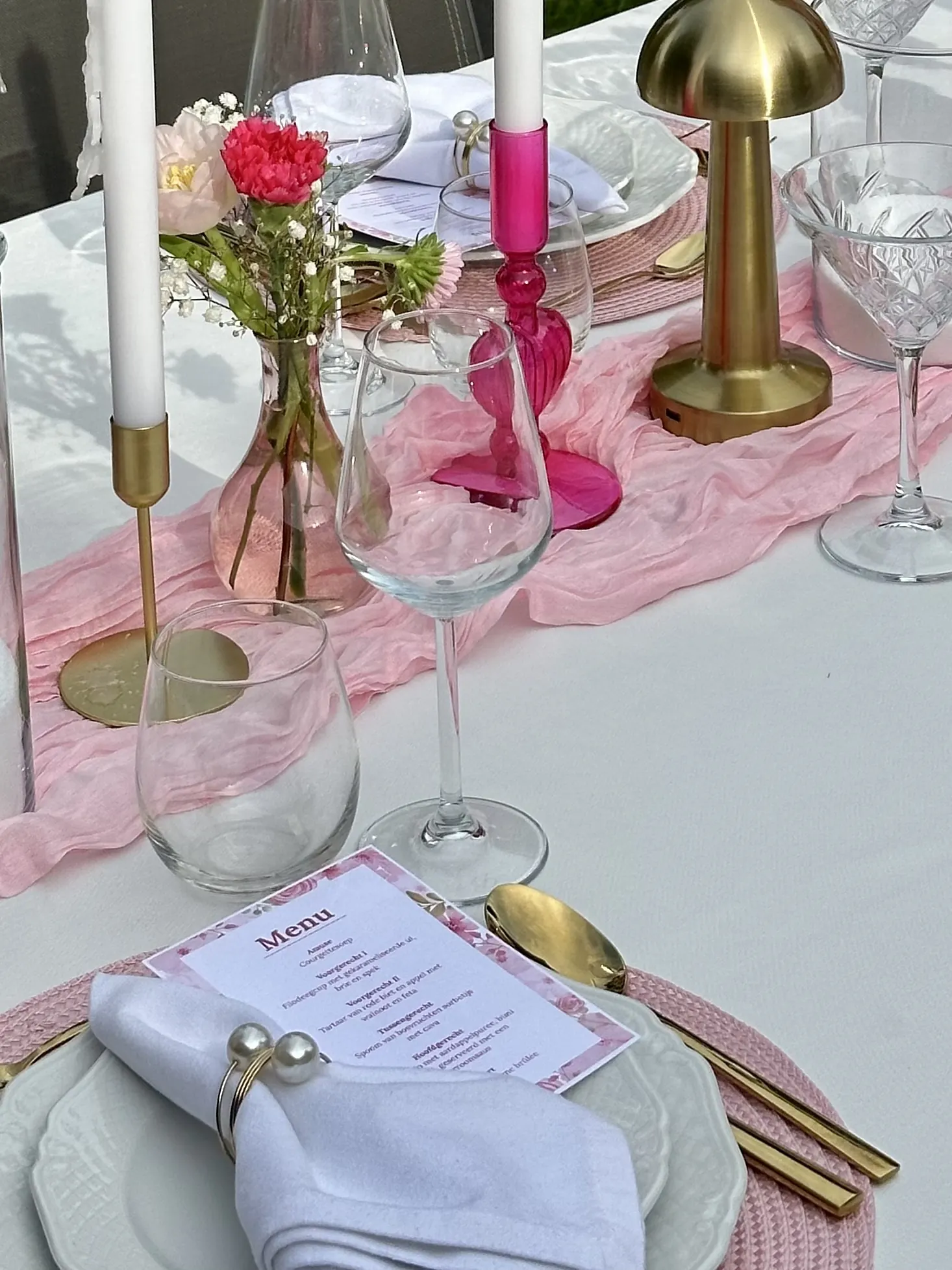 Roze menukaart, een roze glazen kandelaar en bloemen in een roze vaasje