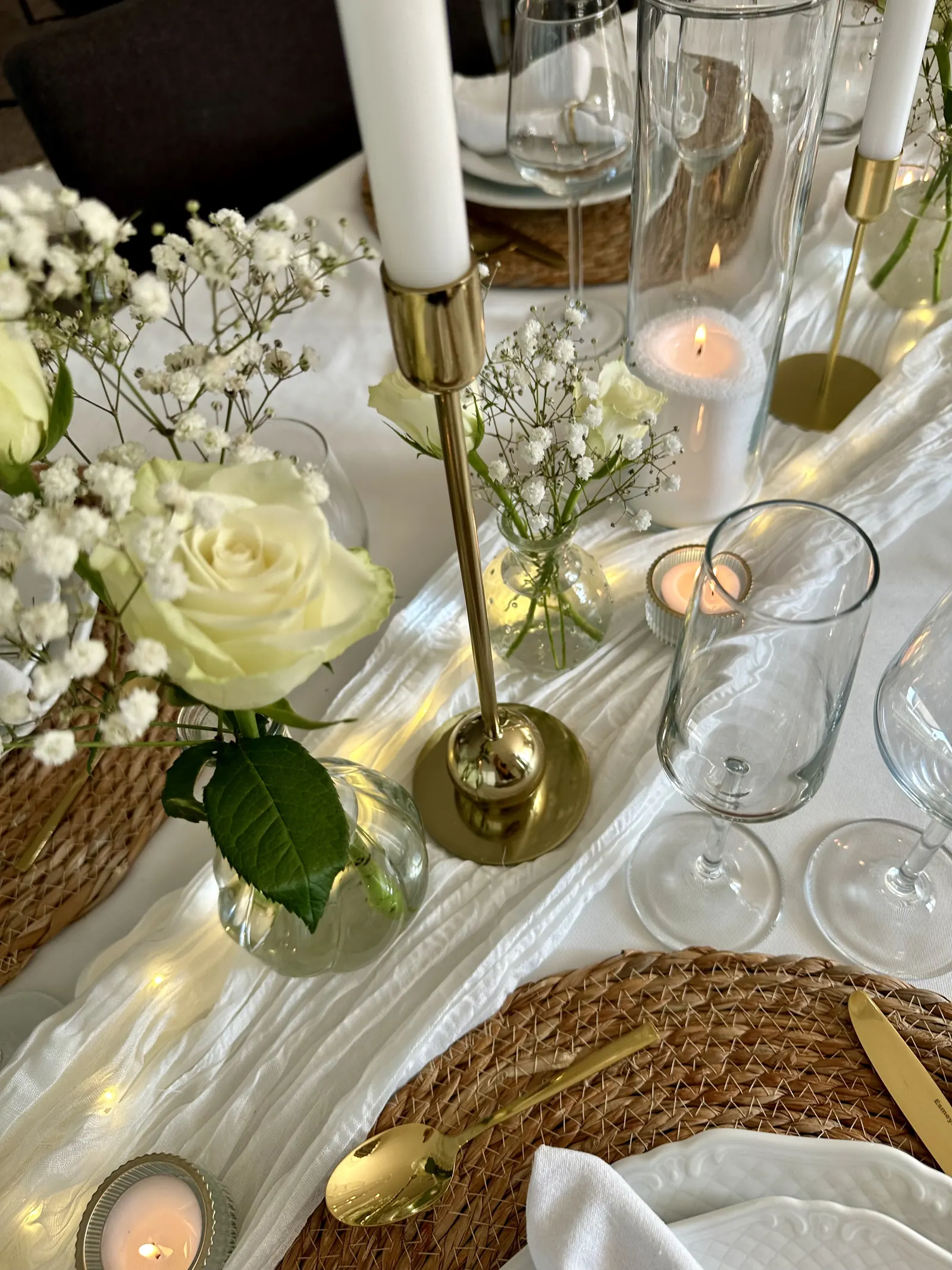 Witte roos in een glazen vaasje naast een gouden kandelaar met een witte kaars